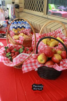 two baskets filled with apples and strawberries on top of a red cloth covered table