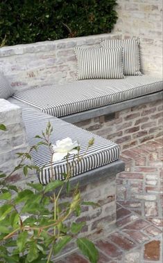 a white rose sitting on top of a bench next to a brick wall and bushes