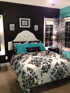 a bedroom with black and white bedding, teal pillows and pictures on the wall