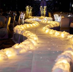 a long table covered in white cloths and lit up with candles on top of it