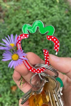 a person holding several keys in front of a purple flower and some green leaves with polka dots on them