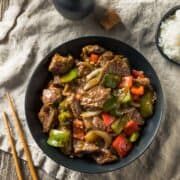 a bowl filled with beef and vegetables next to chopsticks on top of a table