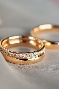 two gold wedding rings sitting on top of a white cloth covered tablecloth, with diamonds in the middle