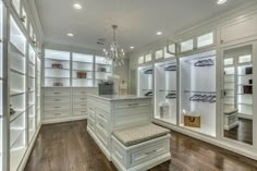 a walk - in closet with white cabinets and glass doors, chandelier hanging from the ceiling