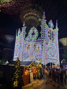 people are walking around in front of a building with lights and decorations on it at night