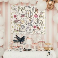 a table topped with cakes and desserts next to white balloons in front of a wall