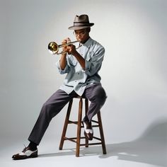 a man sitting on top of a stool holding a trumpet in his right hand and wearing a hat