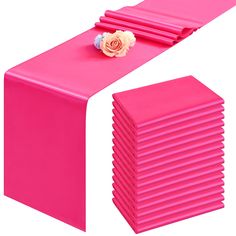 a pink table runner with a flower on top and several folded napkins in the middle