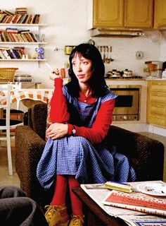 a woman sitting on a couch in a living room next to a table with books