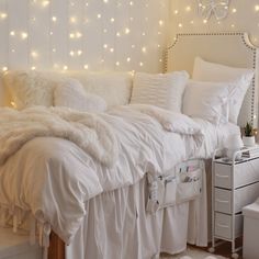 a white bed topped with lots of pillows next to a wall covered in string lights