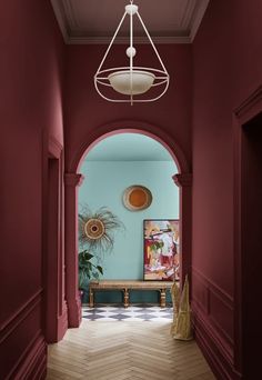 a hallway with red walls and wooden floors, an archway leading to the dining room