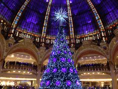 a large christmas tree in the middle of a shopping mall with lights on it's ceiling