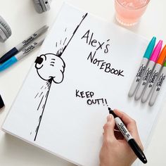 a person writing on a notebook with markers