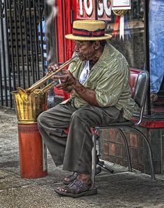 an old man sitting on a bench playing a trumpet in front of a storefront