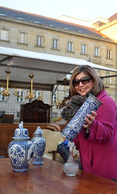 a woman in sunglasses is holding a blue and white vase on a table with other decorative items