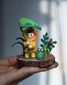 a hand holding a small figurine of a person with an umbrella and plants