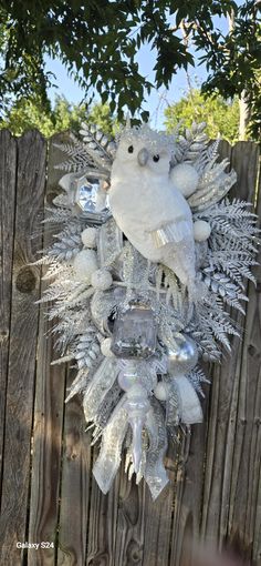 a white teddy bear sitting on top of a snowflake wreath in front of a wooden fence