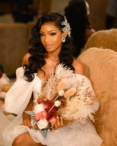 a woman sitting on a chair with flowers and feathers in her hair, wearing a bridal gown