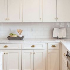 a kitchen with white cabinets and marble counter tops, an open book on the counter