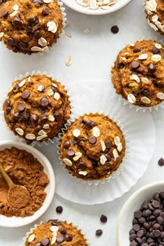 several muffins with chocolate chips and oats in bowls next to them on a white surface