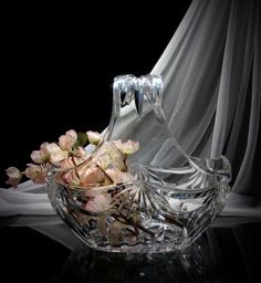 a glass bowl filled with flowers on top of a black table next to a white curtain