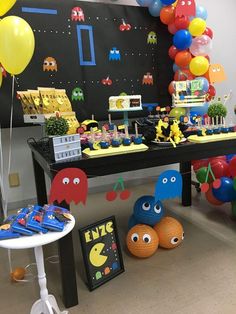 a table topped with balloons and toys next to a blackboard covered in pacman faces