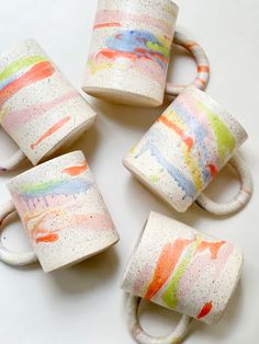 four coffee cups with different colors and designs painted on them, sitting next to each other