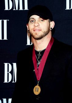 a man in a black suit and hat with a medal around his neck standing on a red carpet