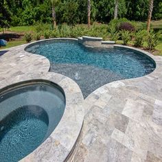 an outdoor swimming pool surrounded by stone patios and landscaping area with trees in the background