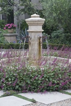 a water fountain surrounded by purple flowers and greenery