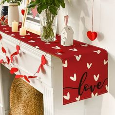 a red table runner with hearts on it and flowers in vases next to the mantle