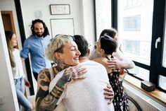 a group of people standing around each other in a room with large windows and lots of tattoos on their arms