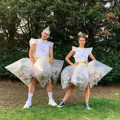 two people dressed in plastic bags standing on grass with trees in the background and bushes behind them