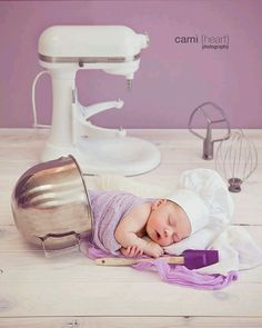 a baby laying on top of a table next to a mixer