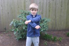 a young boy standing in front of a bush holding his arms out to the side