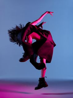 a woman is dancing in the air with her arms spread out and legs bent forward