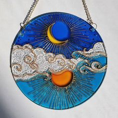 a glass sun and moon hanging from a chain on a white wall with clouds, stars and the moon in the sky