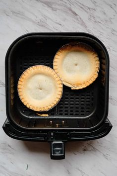 two pies sitting in an air fryer on top of a marble countertop