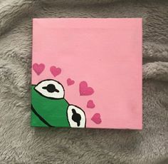 a painting of a green frog with hearts on it's face and pink background