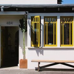 a bench in front of a white building with yellow windows and bars on the doors