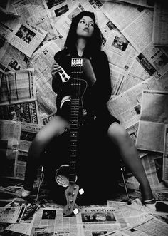 a woman sitting on top of a pile of newspapers holding a guitar in her hands