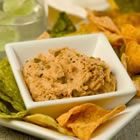 a white bowl filled with dip surrounded by tortilla chips