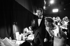 a man in a tuxedo standing next to a woman at a table with other people