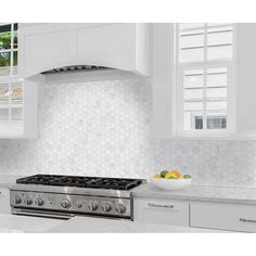 a bowl of fruit sits on the stove top in this white kitchen with hexagonal tile