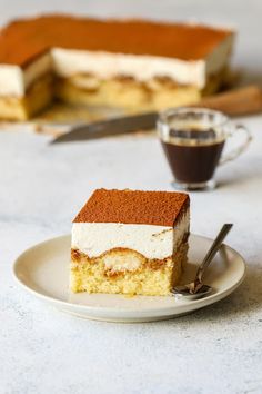 a piece of cake sitting on top of a white plate next to a cup of coffee