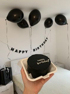 a person holding up a black birthday cake in front of balloons that say happy birthday