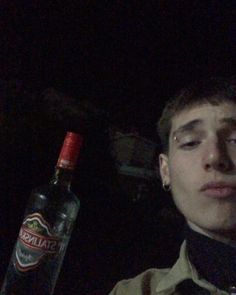 a young man with his eyes closed next to a bottle of alcohol in the dark