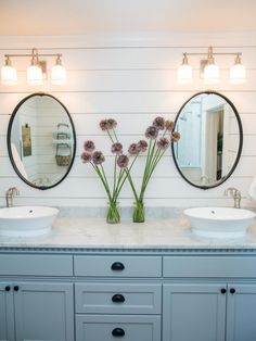 there are two sinks in the bathroom with mirrors on the wall and flowers in vases next to them