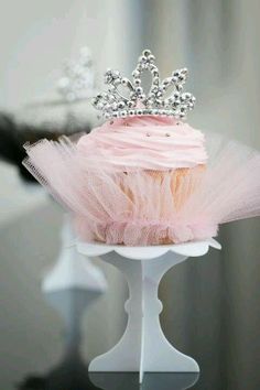 a cupcake with pink frosting and a tiara on top is sitting on a stand