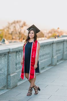 a woman wearing a graduation cap and gown standing on a bridge with her hand in her pocket